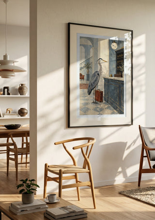 The Heron Checks In by Matthews Gallerie in a black frame in a bright dining room with wooden chairs