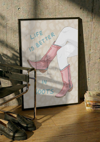 Life is better in boots by Lisen Vennesland in a black frame leaning against a concrete wall by a steel chair