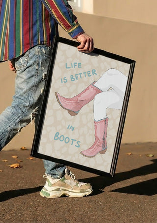 Life is better in boots by Lisen Vennesland carried in a black frame along a sunny street