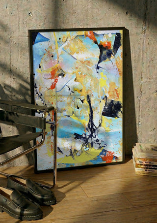 Composition Yellow on Blue by Andreas Pohle in a black frame leaning against a concrete wall by a steel chair