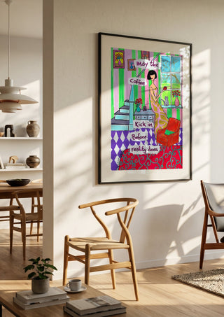 May the Coffee Kick In by Camilla Nilsson in a black frame in a bright dining room with wooden chairs