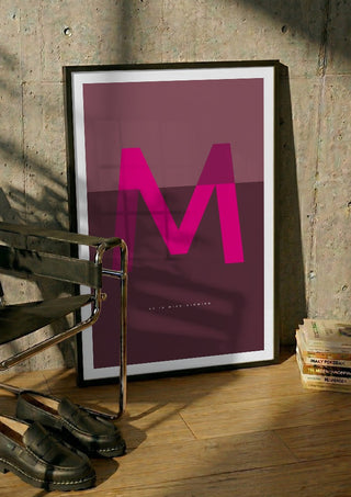 M as in Mind-blowing – Cerise by Quite Nice Prints in a black frame leaning against a concrete wall by a steel chair
