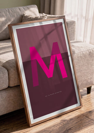 M as in Mind-blowing – Cerise by Quite Nice Prints in a walnut frame leaning against a grey sofa
