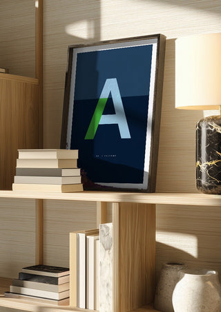 A as in Awesome – Blue by Quite Nice Prints in a dark frame on a wooden shelf beside books and a lamp