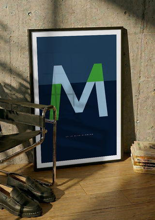M as in Mind-blowing – Blue by Quite Nice Prints in a black frame leaning against a concrete wall by a steel chair