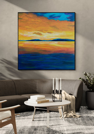 Under An Evening Sky by Finbar Stevens in a black frame above a grey sofa with candlesticks on a round table
