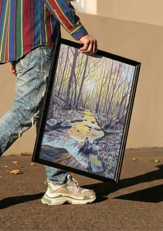 The Evening Stream by Finbar Stevens carried in a black frame along a sunny street
