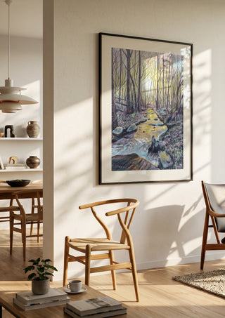 The Evening Stream by Finbar Stevens in a black frame in a bright dining room with wooden chairs