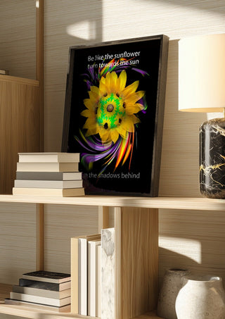 Be like the sunflower by Walter Zettl in a dark frame on a wooden shelf beside books and a lamp