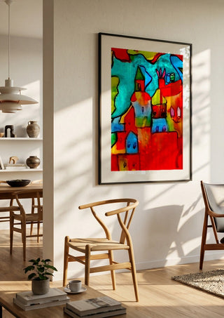 The Village by Nittaart in a black frame in a bright dining room with wooden chairs