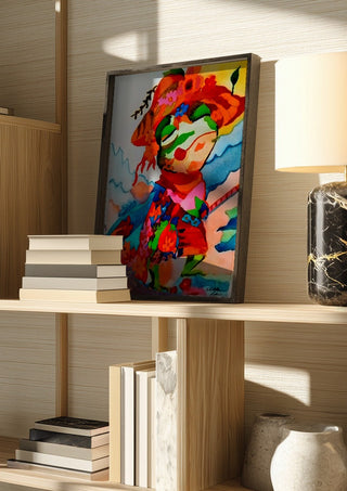 The little frog by Nittaart in a dark frame on a wooden shelf beside books and a lamp