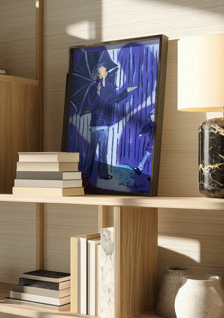 Tanz durch den Regen by Trude in a dark frame on a wooden shelf beside books and a lamp