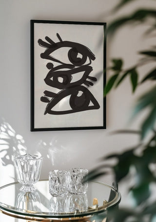 Abstract line art eyes 3 by ThingDesign in a black frame above a glass table with crystal glassware