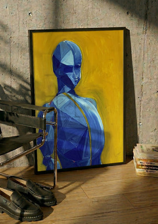 Blue figure / yellow field by Linor Citaku in a black frame leaning against a concrete wall by a steel chair