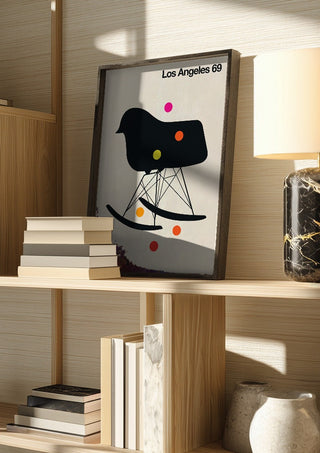 Los Angeles 69 by Bo Lundberg in a dark frame on a wooden shelf beside books and a lamp