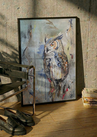 Owl by Lüba in a black frame leaning against a concrete wall by a steel chair