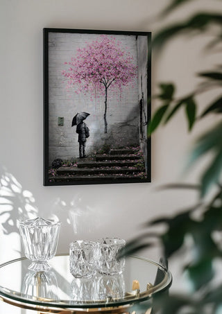 Spring x Banksy by Decker Studios in a black frame above a glass table with crystal glassware