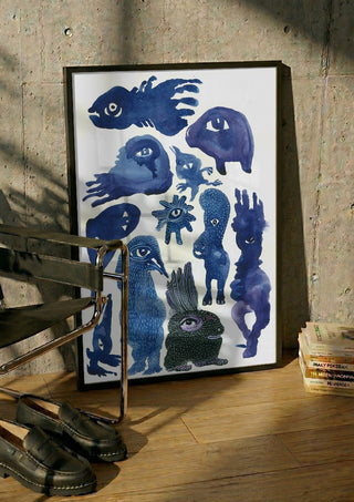 Creatures 2 by Lena Galé in a black frame leaning against a concrete wall by a steel chair