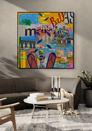 Ciao Bellas by María Burgaz in a black frame above a dark grey sofa with a candle holder
