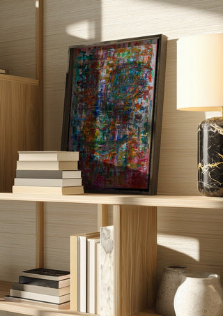 Augenblick by ullimcart in a dark frame on a wooden shelf beside books and a lamp