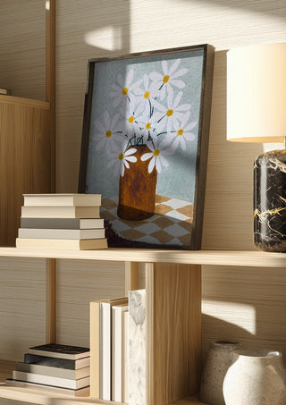 Rutig duk med brun vas by Rebecka Hansson in a dark frame on a wooden shelf beside books and a lamp