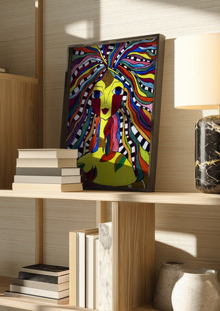 Kaleidoscopic Minds by Bibi in a dark frame on a wooden shelf beside books and a lamp