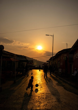Soccer on the street by Gloria Mwivanda - a boy with a ball silhouetted on a golden street at sunset
