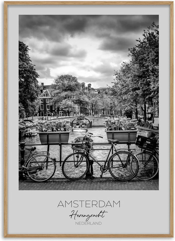 Black and white photo of bicycles by a canal on Herengracht, Amsterdam, with trees and buildings in the background.